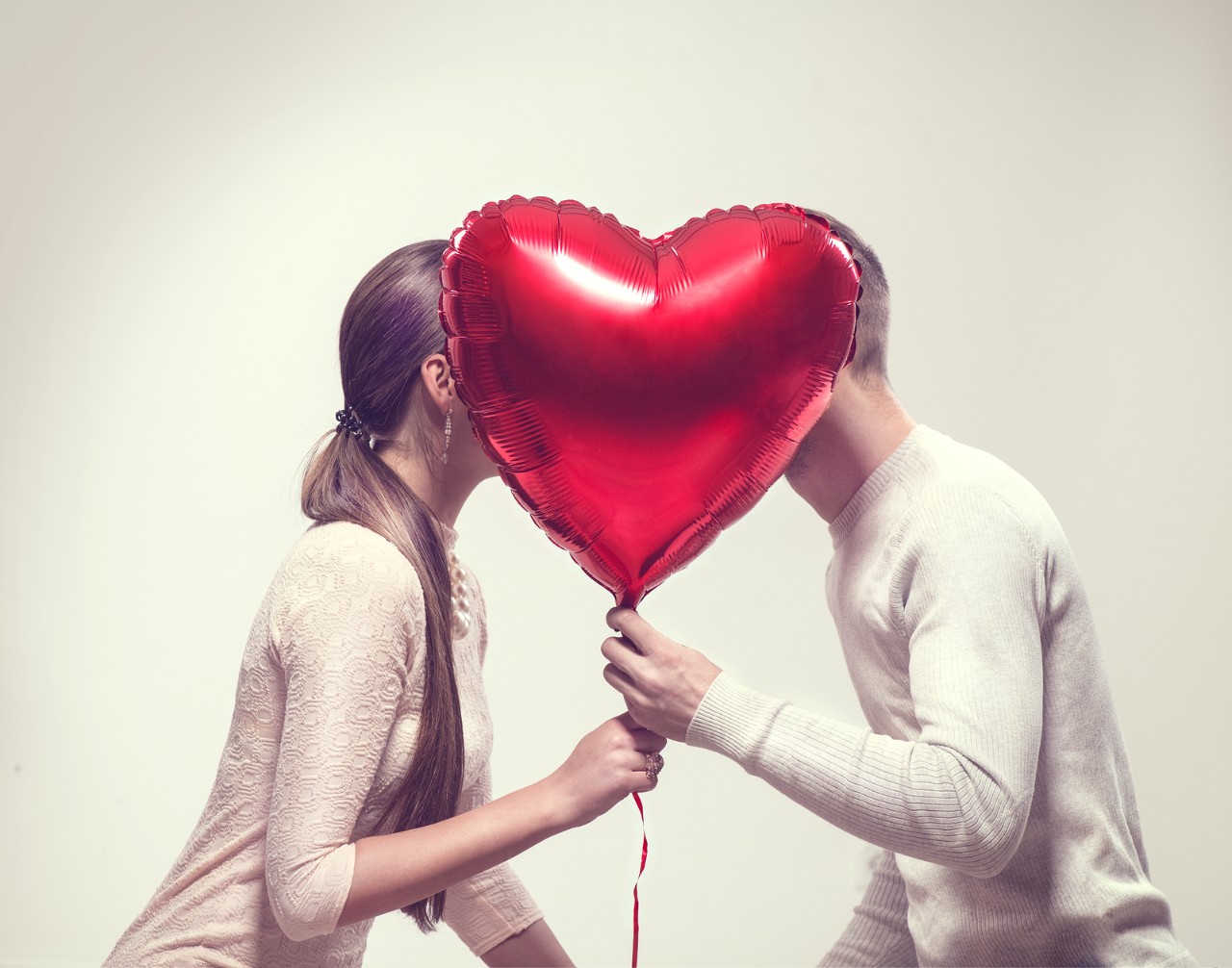 Valentine Couple. Beauty Girl and her Handsome Boyfriend holding heart shaped air balloon and kissin