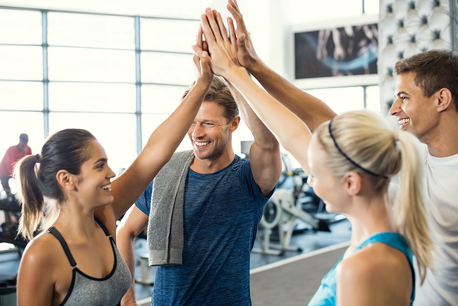 Smiling men and women doing high five in gym. Group of young people making high five gesture in gym 