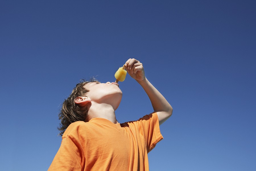 Low angle view of a little boy eating popsicle against clear blue sky